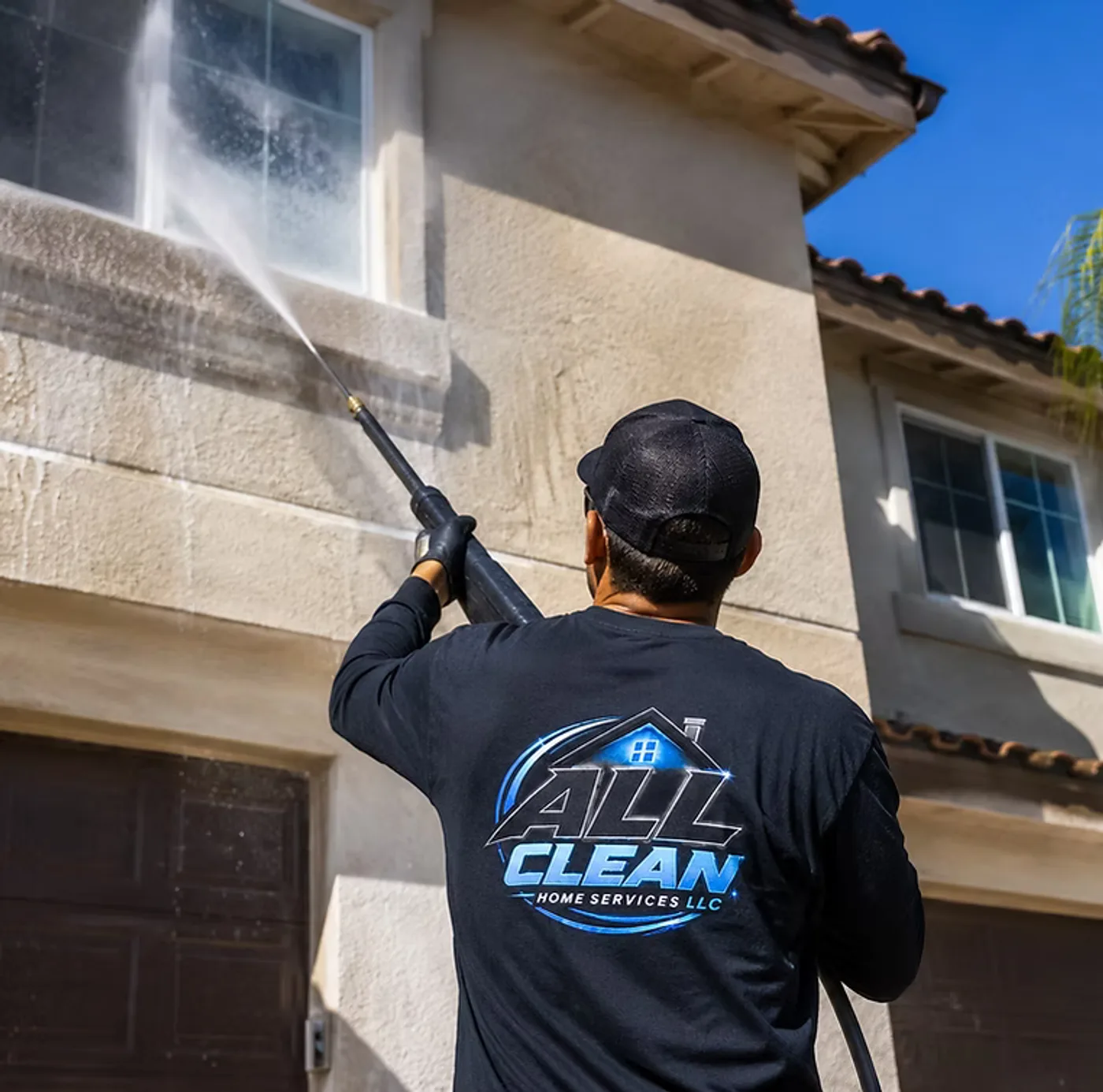 ALLCLEAN Home Services crew member in a company shirt washing the stucco exterior of a home
